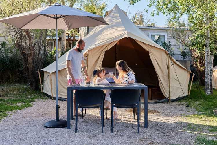 Familia disfrutando en una mesa frente al glamping Bell Tent Balsa en TAIGA Delta de l'Ebre, España.