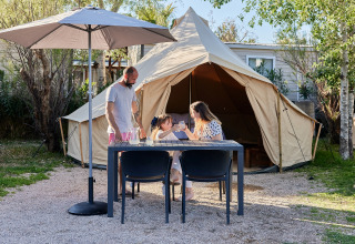 Familie entspannt an einem Tisch vor dem Glamping Bell Tent Balsa bei TAIGA Delta de l'Ebre in Spanien.