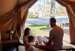 Een gezin leest samen in een Glamping Bell Tent Balsa bij TAIGA Delta de l'Ebre in Spanje.