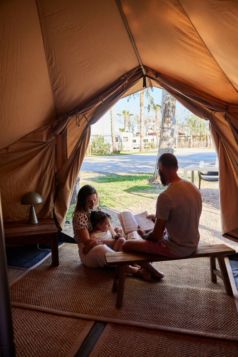 Een gezin leest samen in een Glamping Bell Tent Balsa bij TAIGA Delta de l'Ebre in Spanje.