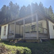 Chalet Pauline van buitenaf met houten terras, grasveld en bosrijke achtergrond in de zon.