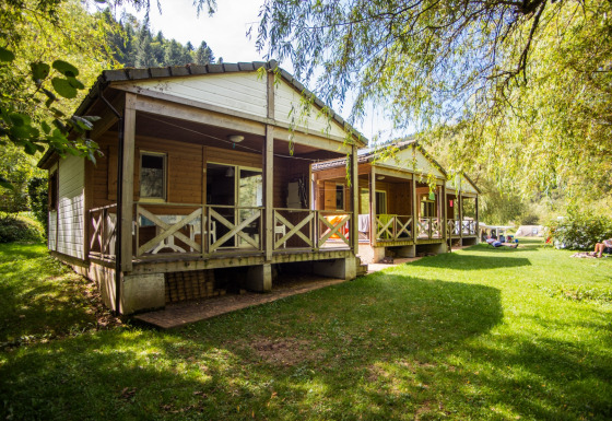 Træchalet kaldet Chalet confort med udsigt over floden, omgivet af grøn natur og afslappede gæster.