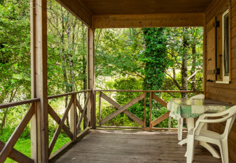 Træveranda med udsigt til flod og grøn skov ved Chalet confort, Centre de Vacances Tariche, Schweiz.