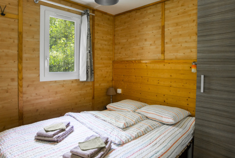 Bedroom with wooden walls and double bed in Chalet confort (river view) at Centre de Vacances Tariche, Switzerland.