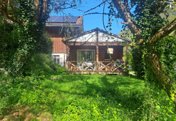 Chalet confort with wooden terrace, lush greenery, sunshine, blue sky and stream view from the garden.
