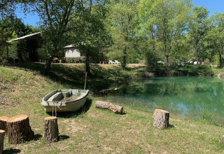 Barque au bord d’une mare paisible, troncs pour s’asseoir et arbres au Flower Camping La Rivière en France.