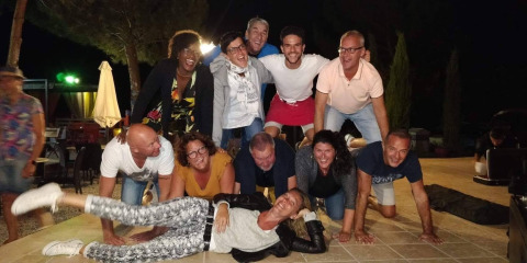 Gruppo di adulti sorridenti forma una piramide umana al Flower Camping La Rivière in Provenza, Francia, di sera.