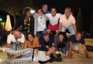 Gruppo di adulti sorridenti forma una piramide umana al Flower Camping La Rivière in Provenza, Francia, di sera.