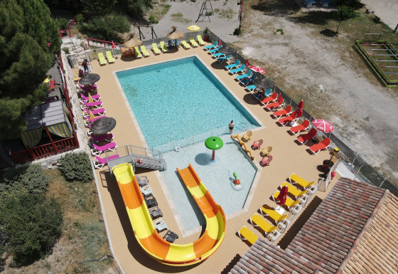 Luftaufnahme eines Pools mit Wasserrutsche und Sonnenliegen im Flower Camping La Rivière in Provence, Frankreich.