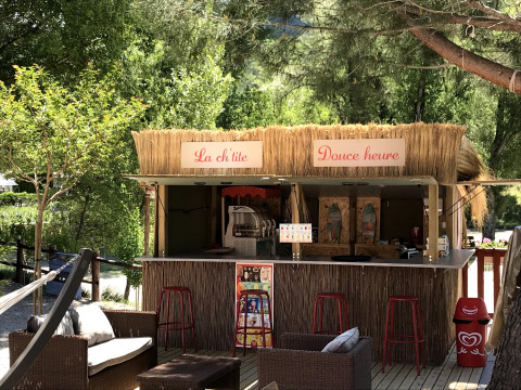 Snack-bar en plein air au toit de chaume avec tabourets rouges à Flower Camping La Rivière en Provence-Alpes-Côte d’Azur.