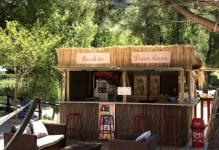 Udendørs snackbar med stråtag og siddepladser i skyggefulde omgivelser ved Flower Camping La Rivière i Frankrig.