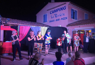 En gruppe optræder på en udendørs scene ved Flower Camping La Rivière, Provence, foran publikum.