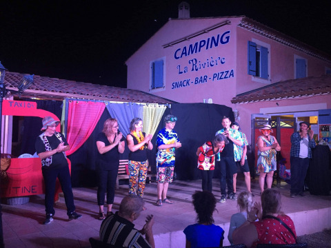 En gruppe optræder på en udendørs scene ved Flower Camping La Rivière, Provence, foran publikum.