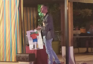 Un uomo mostra un disegno ai bambini durante uno spettacolo serale al Flower Camping La Rivière in Francia.
