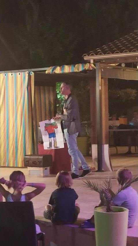 Un uomo mostra un disegno ai bambini durante uno spettacolo serale al Flower Camping La Rivière in Francia.