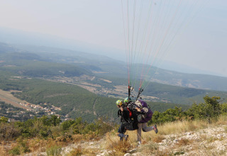 To personer paragliding fra en bakke med udsigt over landskabet nær Flower Camping La Rivière i Frankrig.