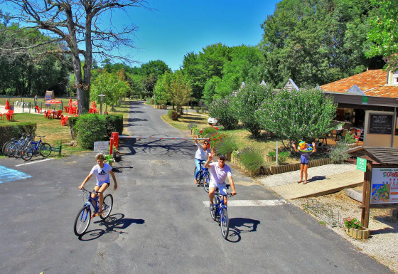 Feriepark Camping Le Périgord i Nouvelle-Aquitaine, Frankrig, med cyklende familier, grønne træer og udendørs aktiviteter.