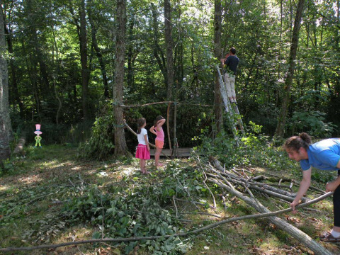 Familia construyendo un refugio de ramas en el bosque de Camping Le Périgord, Francia, niños y adultos juntos.