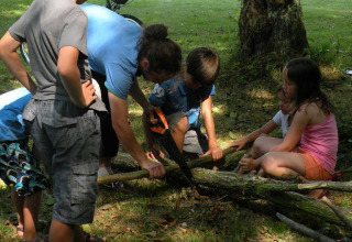 Børn og voksen saver trægrene sammen i skyggen på Camping Le Périgord i Nouvelle-Aquitaine, Frankrig.