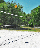 Dos niños juegan al voleibol en una cancha de arena rodeada de árboles en Camping Le Périgord, Nouvelle-Aquitaine, Francia.