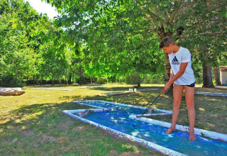 Ung dreng spiller minigolf i solen omgivet af grønne træer på Camping Le Périgord, Nouvelle-Aquitaine, Frankrig.