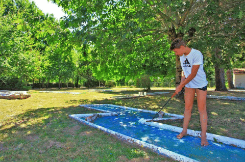 Un ragazzo gioca a minigolf a piedi nudi tra gli alberi al Camping Le Périgord, Nouvelle-Aquitaine, Francia.