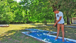 Un ragazzo gioca a minigolf a piedi nudi tra gli alberi al Camping Le Périgord, Nouvelle-Aquitaine, Francia.