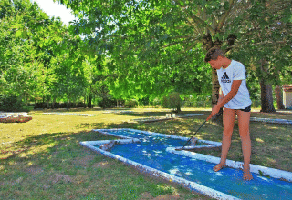 Un ragazzo gioca a minigolf a piedi nudi tra gli alberi al Camping Le Périgord, Nouvelle-Aquitaine, Francia.