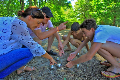 Cuatro personas juegan a la petanca y comparan posiciones de bolas en Camping Le Périgord bajo el sol.