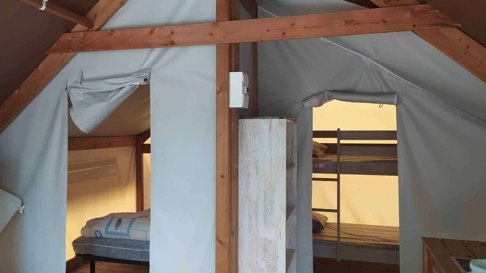 Interieur van de Ecolodge toilé Standard bij Flower Camping La Rivière in Frankrijk met stapelbedden en houten balken.