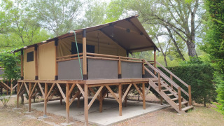 Verhoogde Lodge op palen Confort met houten en canvas structuur te midden van een groene, bosrijke natuur.