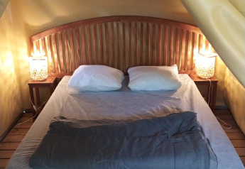Cozy bedroom with double bed, wood headboard, lamps, and wood floor at Lodge op palen Confort in France.
