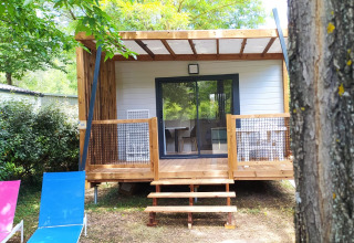 Chalet Cajou Confort al Flower Camping La Rivière in Francia, circondato da alberi e natura.