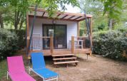 Chalet Cajou Confort avec terrasse en bois et chaises longues, entouré de verdure et de haies.