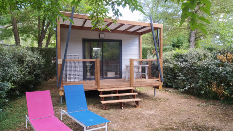 Chalet Cajou Confort met houten veranda en loungestoelen in de tuin, verscholen tussen groene struiken.