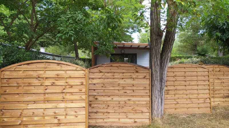 Houten schutting voor een chalet bij Chalet Cajou Confort, Flower Camping La Rivière, omgeven door bomen.