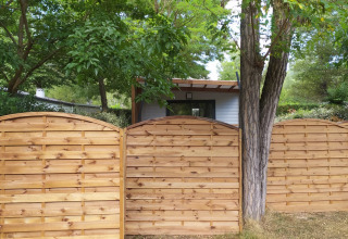 Holzzaun vor einem Chalet bei Chalet Cajou Confort auf Flower Camping La Rivière, umgeben von Bäumen.