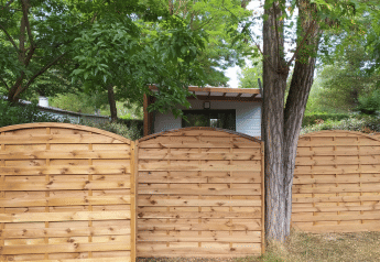 Holzzaun vor einem Chalet bei Chalet Cajou Confort auf Flower Camping La Rivière, umgeben von Bäumen.