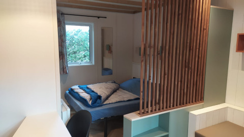 Interieur van Chalet Cajou Confort op Flower Camping La Rivière in Frankrijk met bed en houten afscheiding.