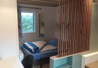 Interieur van Chalet Cajou Confort op Flower Camping La Rivière in Frankrijk met bed en houten afscheiding.