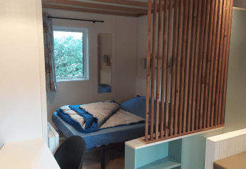 Interieur van Chalet Cajou Confort bij Flower Camping La Rivière in Frankrijk met bed en houten schutting.