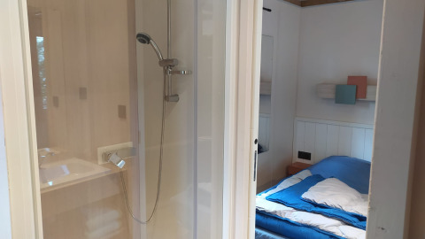 Habitación con cama y ducha en el Chalet Cajou Confort de Flower Camping La Rivière en Francia.