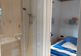 Habitación con cama y ducha en el Chalet Cajou Confort de Flower Camping La Rivière en Francia.