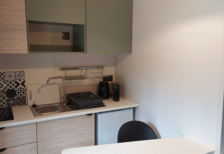 Moderne compacte kitchenette in Chalet Cajou Confort met spoelbak, kookplaat en zwart afdruiprek.