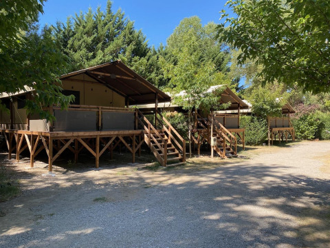 Glamping tenten op verhoogde houten terrassen omgeven door bomen en een blauwe lucht in de natuur.