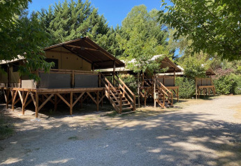 Glamping-Unterkünfte mit erhöhten Holzterrassen und Zelten, umgeben von Bäumen und Sonne.
