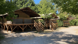 Glamping-Unterkünfte mit erhöhten Holzterrassen und Zelten, umgeben von Bäumen und Sonne.
