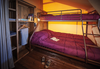 A cozy glamping room featuring a bunk bed with purple bedding, open book, wooden floor, and closet.