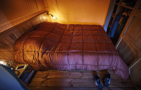 Slaapkamer met een comfy bed en houten inrichting in Lodge op palen Confort 46m² bij Flower Camping La Rivière, Frankrijk.