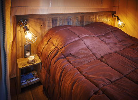 Slaapkamer met bruine dons, houten hoofdbord en rustieke lampen in Lodge op palen Confort 46m², Frankrijk.